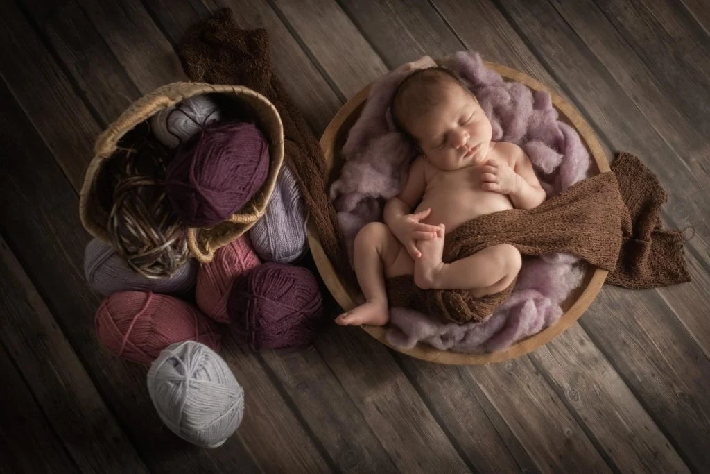 Bebé dormido en una cesta con ovillos de lana y tejidos naturales